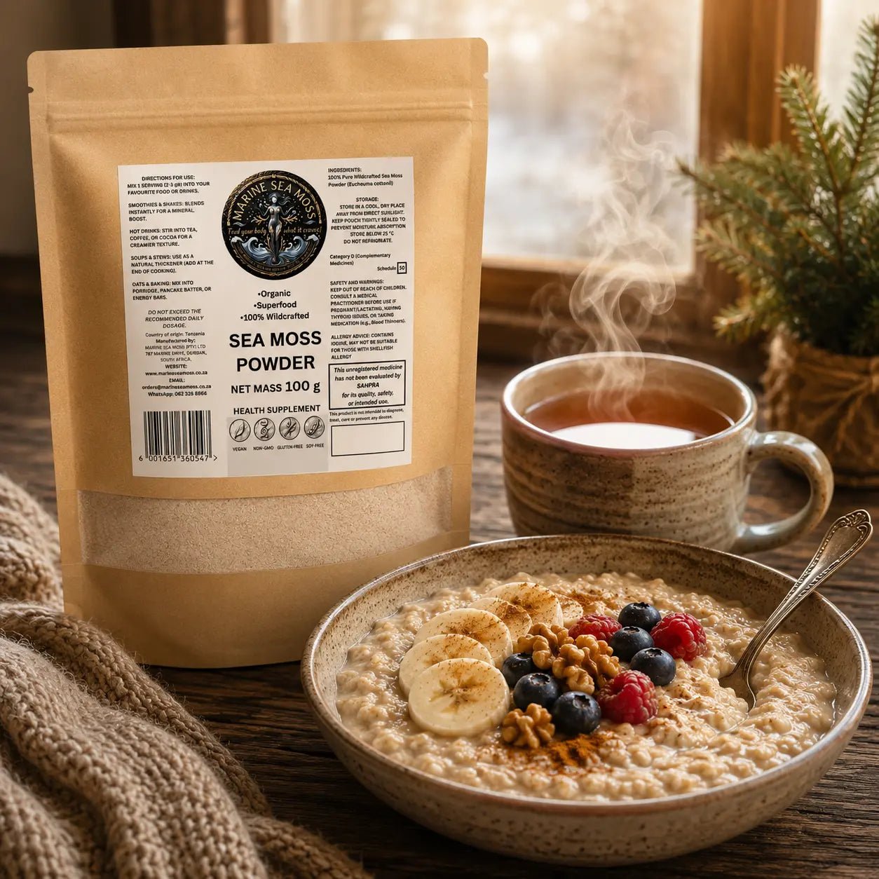 An oatmeal bowl topped with sliced bananas, berries, walnuts, and cinnamon sits next to a steaming mug and a brown paper pouch of "Marine Sea Moss Powder".
