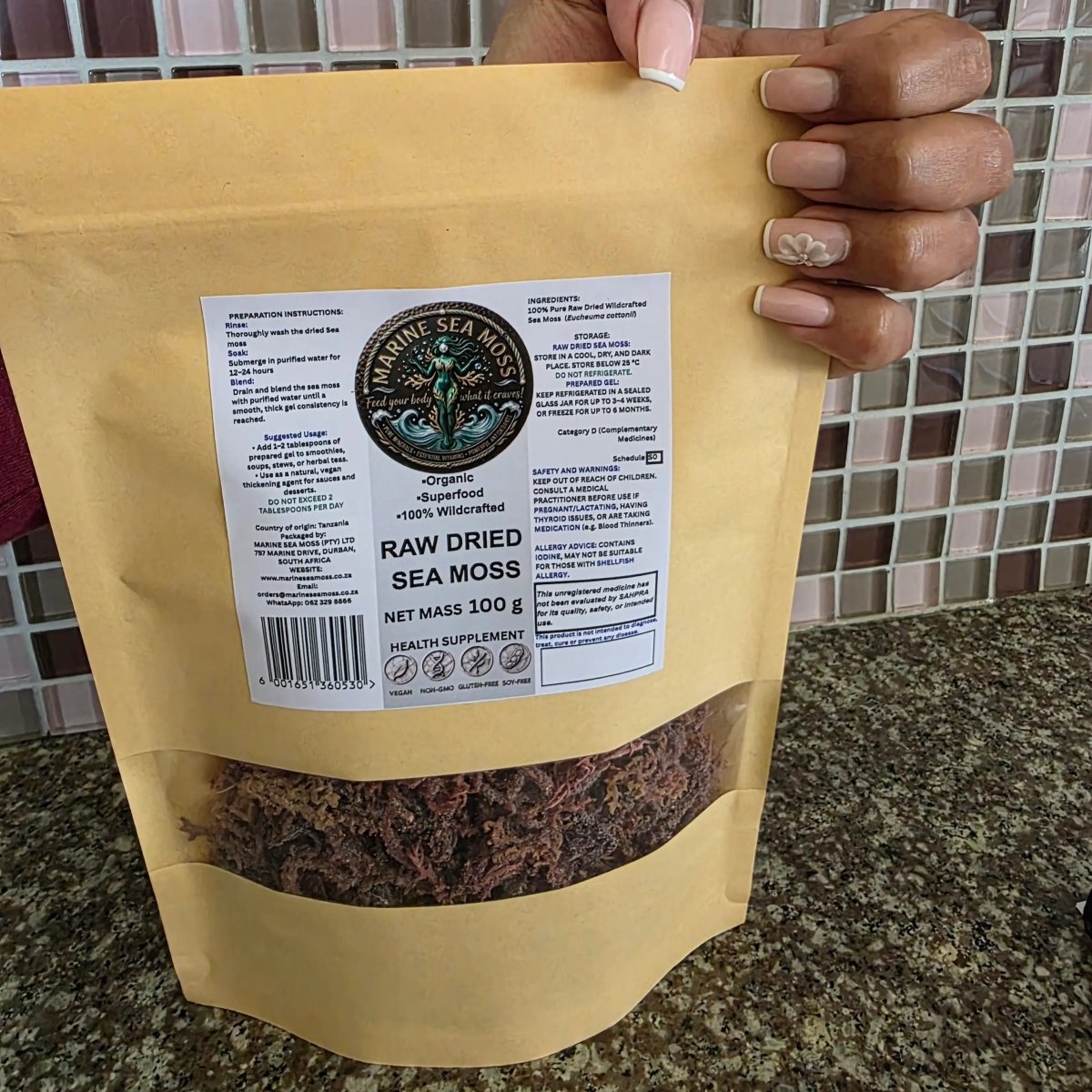 Hand holding Raw Dried Sea Moss 100g pouch showing sea moss through clear window